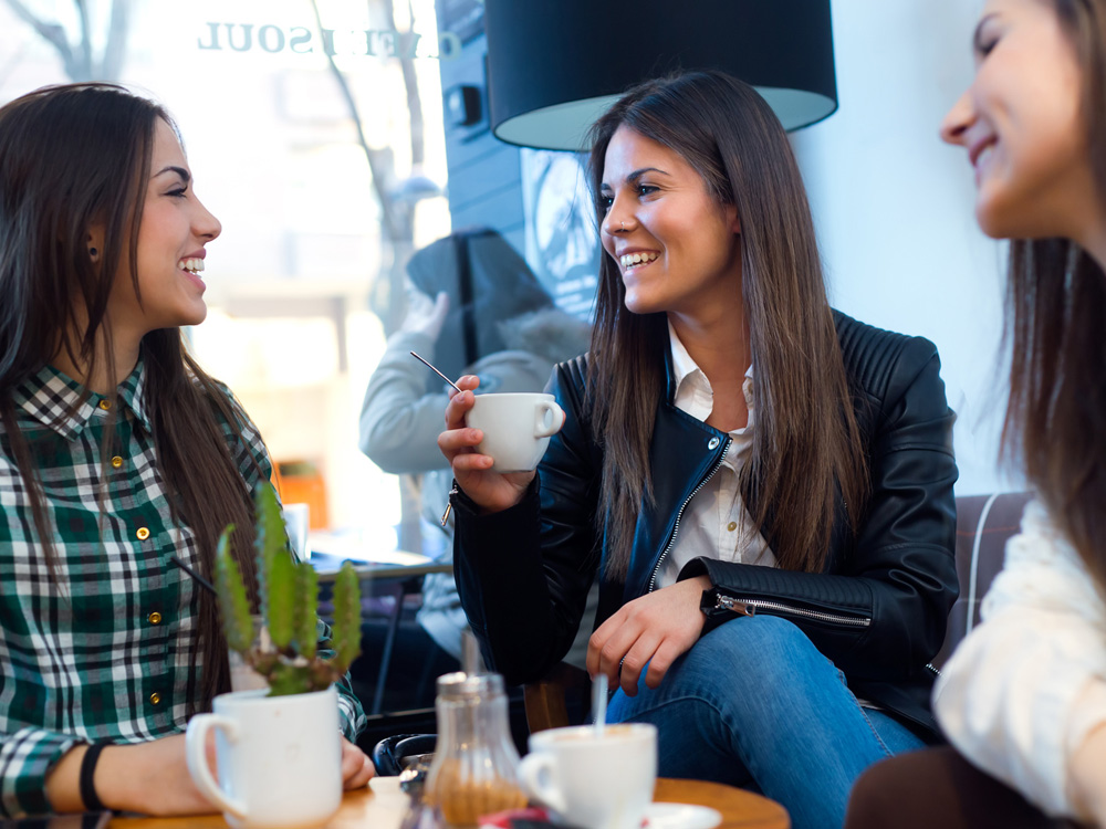 Three young woman drinking coffee and speaking at cafe shop.
